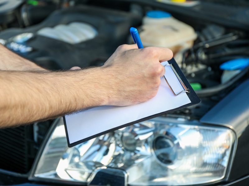 A man in overalls writes to a clipboard. Mechanic. Car inspection